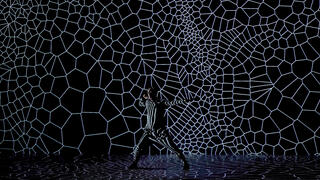 Performer im Dunkeln vor Leinwand, auf die eine Grafik projiziert wird