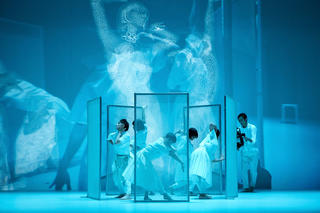 Mehrere Tänzerinnen in Bewegung, im Hintergrund Leinwandprojektionen. 