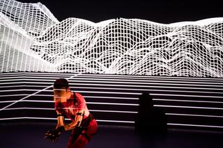 Ein futuristisches Bühnenbild, in dessen Zentrum ein rot gekleideter Darsteller steht.