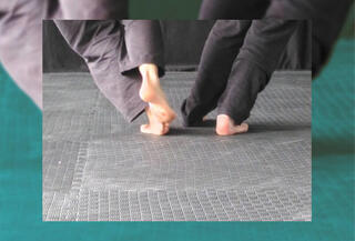 Nackte Füße und deren Unterschenkel zweier Menschen mit grauer und schwarzer Hose laufen auseinander auf grauen Softmatten 