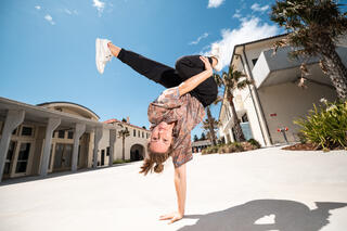 Frieda Frost is in a breaking pose, leaning upside down on one arm