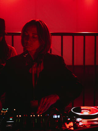 Es ist Amrei zu sehen, wie sie auflegt. Der Raum ist in rotes Licht gefärbt.