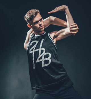 RuffyFlex hält seine Arme verdreht hinter seinem Kopf. Der Hintergrund ist schwarz und er trägt ein schwarzes Tanktop.