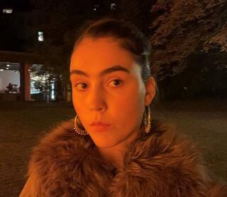 Ein Selfie der Tänzerin Florinda. Sie ist in orangenes Licht getaucht und trägt eine Jacke mit Fellkragen.