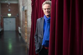 Bertram Müller, einer der Gründer des tanzhauses, tritt aus einem roten Vorhang hervor in den Akademiegang
