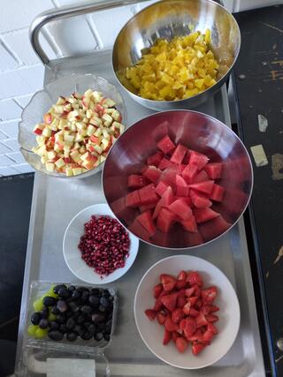 Das Bild bildet einen Servierwagen ab mit vielen Schüsseln mit geschnittenem Obst drauf. Es scheint als wäre dieses für mehrere Menschen vorbereitet worden. 