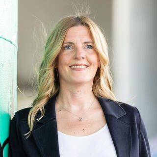 Charlotte Kreft Eine Frau mit offenen blonden Haaren mit weißem Shirt und einem dunklen Blazerschaut schaut lächelnd nach vorne