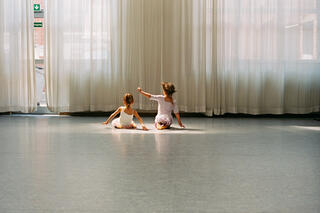 Zwei kleine sitzende Mädchen im Tanzstudio. man sieht sie nur von hinten.