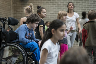 Viele Tänzerinnen und Tänzer im Tanzstudio, in der Mitte ein Junge im Rollstuhl.