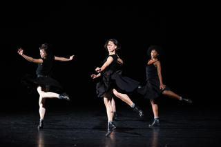 Drei Tänzerinnen auf halber Spitze, schwarz gekleidet und in Bewegung
