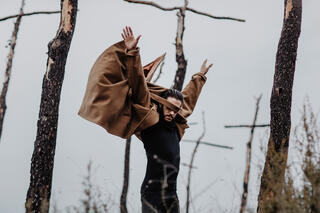 Ein Tänzer steht auf einem Feld mit Holzkreuzen und streckt beide Arme in die Lüfte.