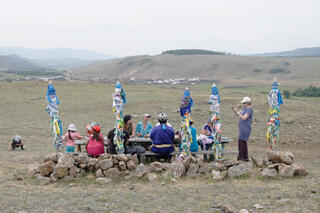 Eine Gruppe Menschen sitzt zwischen Pfeilern in einer Prärie