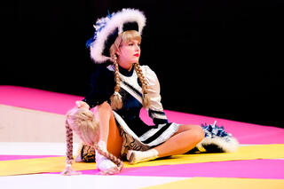 Eine Tänzerin im Funkenmariechen Kostüm hält eine blonde Perücke in der Hand