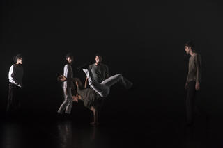 Fünf urbane Tänzer*innen performen auf einer dunklen Bühne.