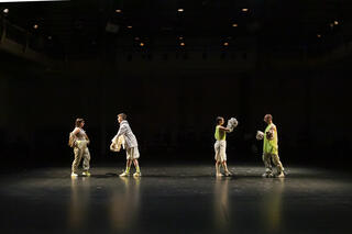Vier Performer*innen tanzen miteinander auf einer schwarzen Bühne