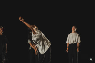 Drei Performer*innen in weißen T-Shirts tanzen miteinander auf der Bühne des tanzhaus nrw.