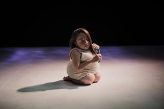 Die Performerin Chiara Bersani kniet auf dem Boden und kämmt sich mit geschlossenen Augen die Haare.