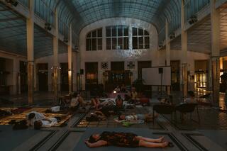 Zu sehen ist eine Gruppe von Personen, die während einer Klang-Séance gemeinsam in einem großen Raum auf dem Boden liegt.