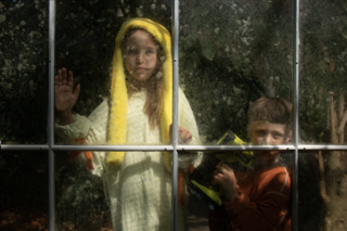 Zwei Kinder stehen nebeneinander und schauen durch eine Glasscheibe mit Rahmen. Eines der Kinder legt seine Hand and die Scheibe und das andere hält eine Taschenlampe.