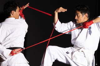 Zwei Tänzer in weißen Kampfanzügen kämpfen mit rotem Seil