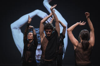 Vier Tänzer halten Arme in die Luft, dahinter Videoprojektion