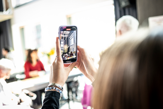 Eine junge Person ist von hinten zu sehen. Sie macht eine Aufnahme mit ihrem Smartphone.