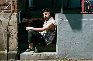 Portraitfoto von Rymon Zacharei aka Rayboom. Rayboom sitzt seitlich auf einer Treppe und hat ein Bein angewinkelt.