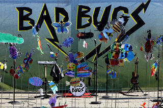 Open Air Bühne mit Schlagzeug usw., davor von Kindern gezeichnete Tiere auf Ständern und auf der Wand im Hintergrund die Worte Bad Bugs